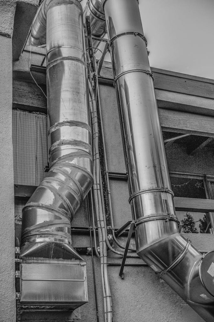pexels photo 10431783 Black and white image showcasing large steel pipes on a building exterior.
